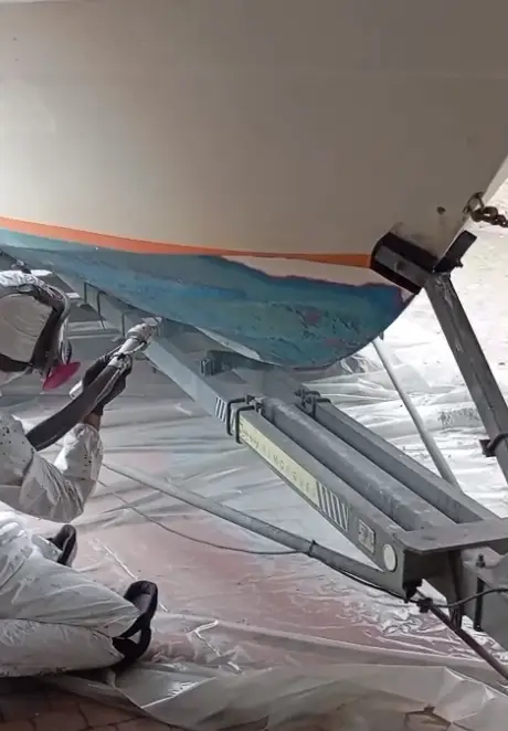 Technicien en train de décaper la peinture antifouling d'une coque de bateau à l'aide d'une sableuse à basse pression.