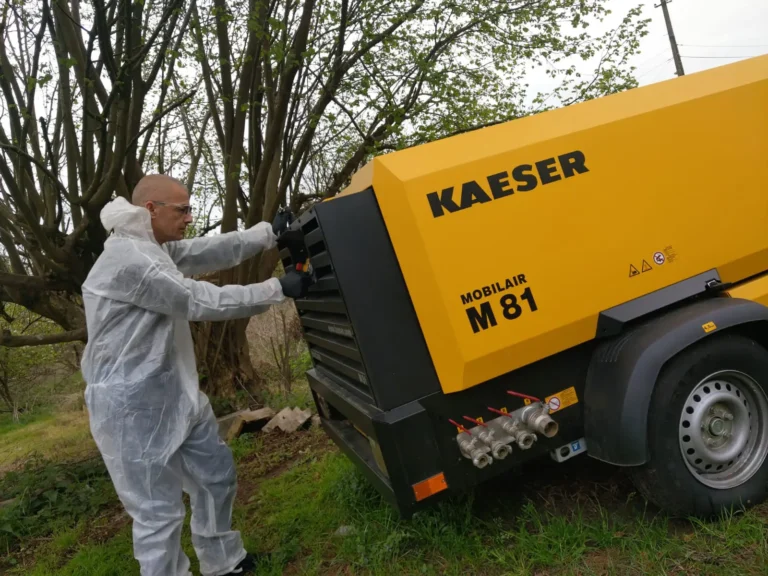 Technicien de Surface Reborn en combinaison de protection, préparant un compresseur de chantier Kaeser MOBILAIR M81 pour une intervention d'aérogommage ou de nettoyage cryogénique.