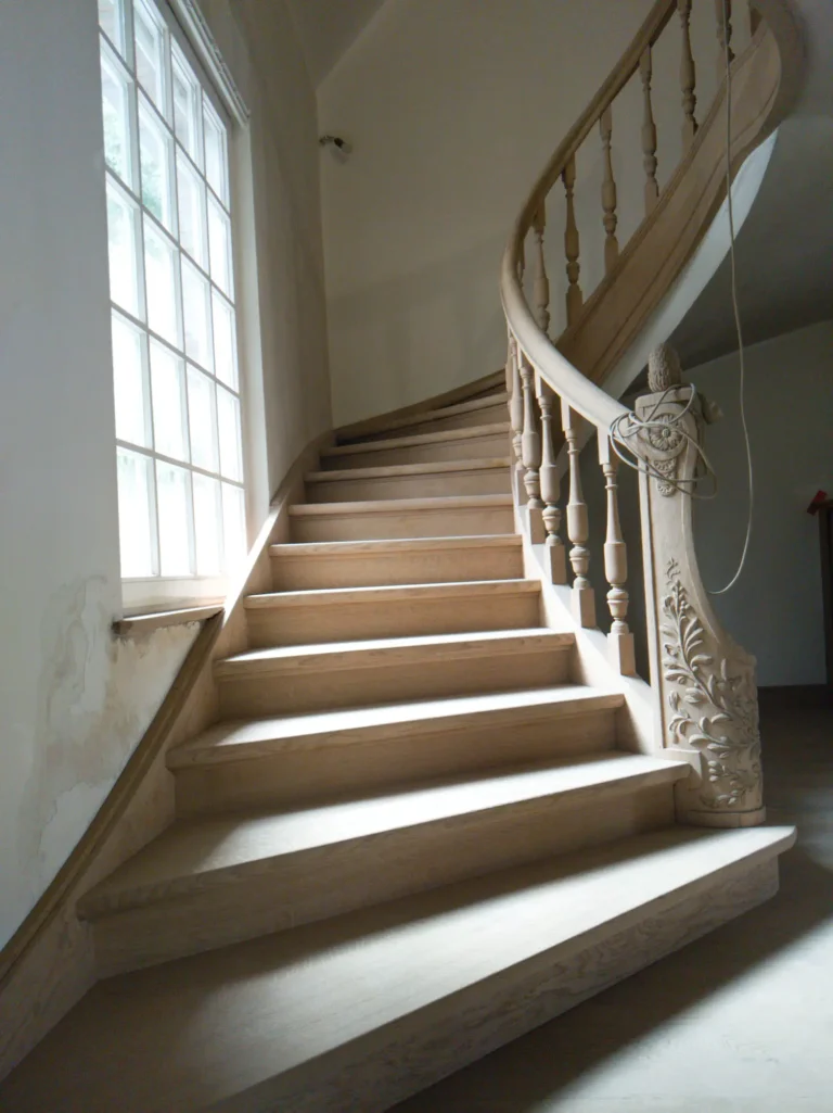 Escalier en bois décapé avec balustres tournés et newel sculpté, lumière naturelle