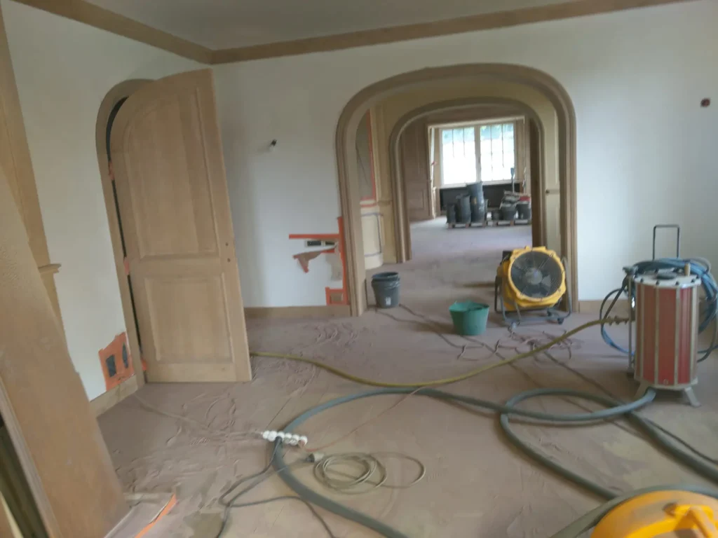 Intérieur de maison de maître en fin de rénovation avec parquet foncé posé, menuiseries en bois massif et murs blancs fraîchement peints.