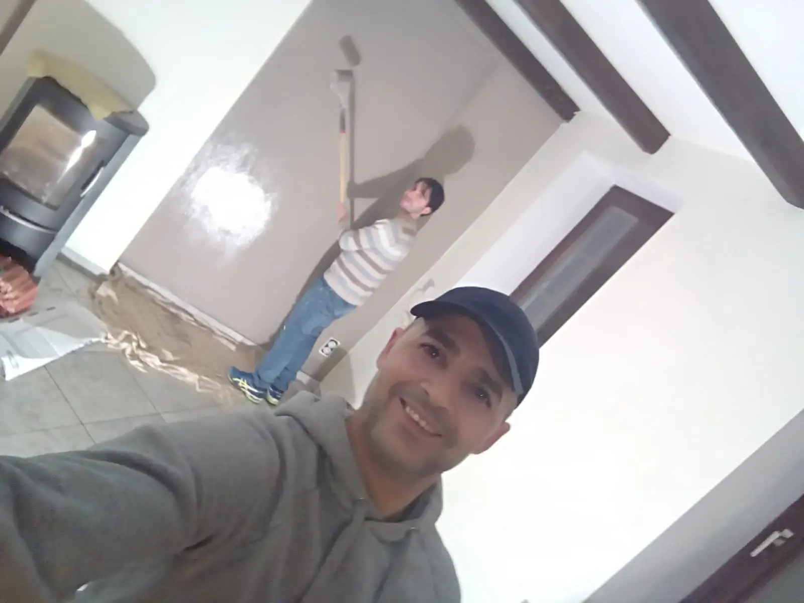 Deux professionnels réalisant des travaux de peinture et de rafraîchissement des murs dans un salon avant un état des lieux de fin de bail.