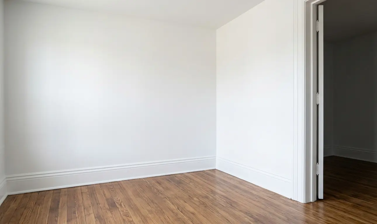 Angle de pièce entièrement rénové avec murs blancs immaculés, parquet propre et porte réparée.