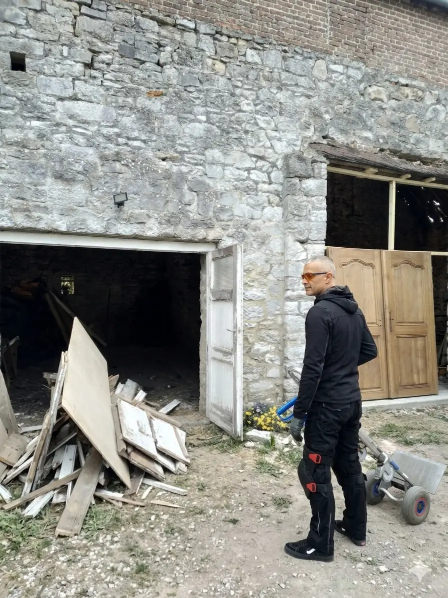Le gérant de Surface Reborn, en équipement de sécurité, inspecte un chantier de rénovation avant location en extérieur, près d'un diable professionnel monte-escalier.
