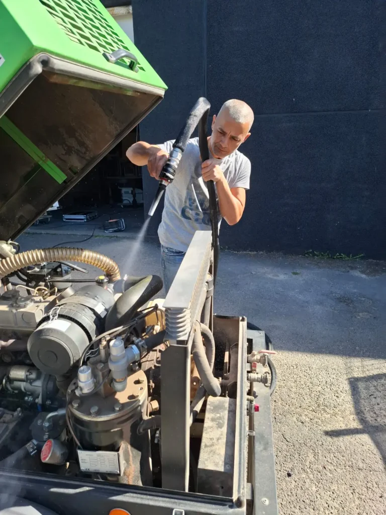 Un technicien de Surface Reborn nettoie un grand compresseur à moteur thermique en utilisant un pistolet de nettoyage cryogénique.
